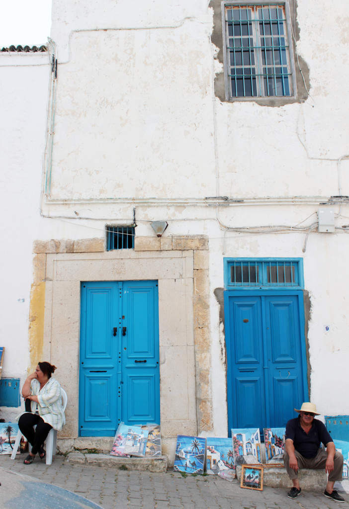 A man and a woman sitting outside houses with two blue doors in the city of Sidi Bou Said, Tunisia.